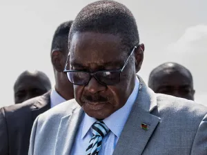 Former Malawi President Peter Mutharika in a grey suit, dark glasses and blue shirt inspects a ballot paper (not visible in the photo) before casting his vote