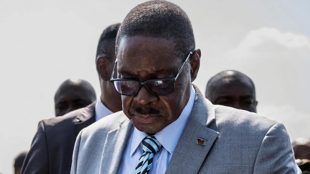 Former Malawi President Peter Mutharika in a grey suit, dark glasses and blue shirt inspects a ballot paper (not visible in the photo) before casting his vote