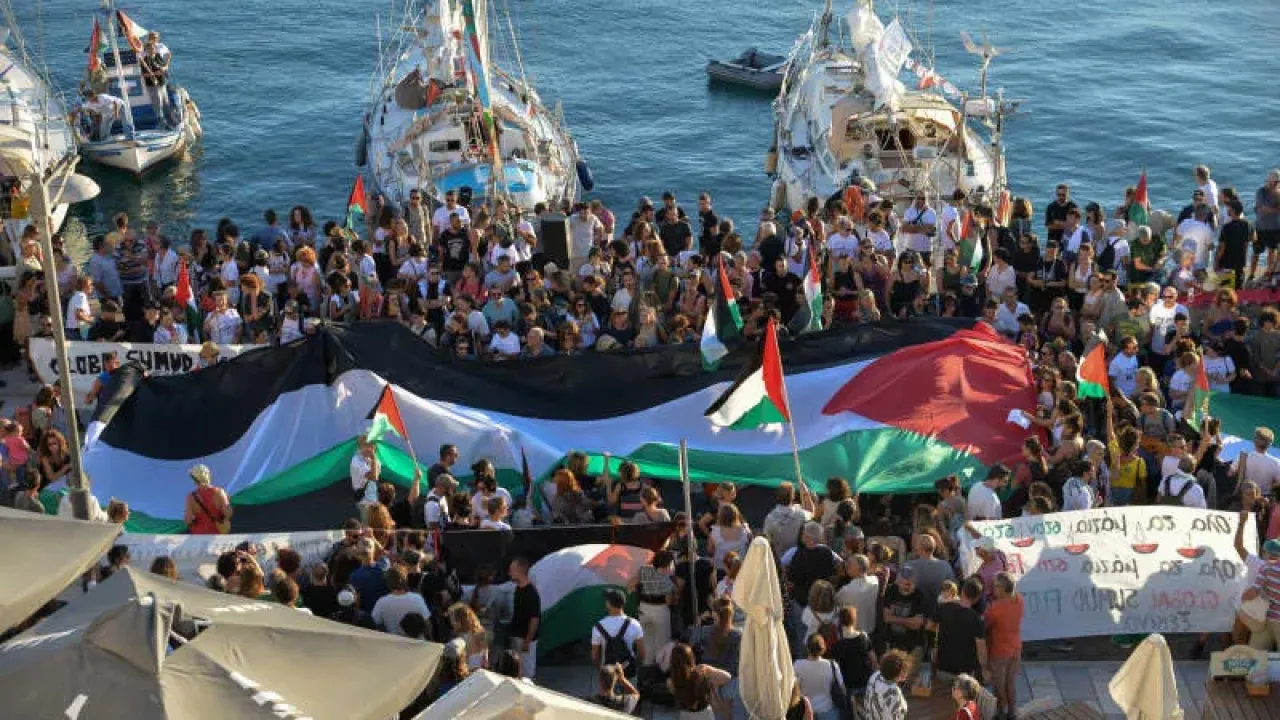 A Palestinian flag is seen as people gather at the port of Ermoupolis before the departure of two sailing boats, Electra and Oxygen, part of the Global Sumud Flotilla aiming to reach Gaza and break Israel