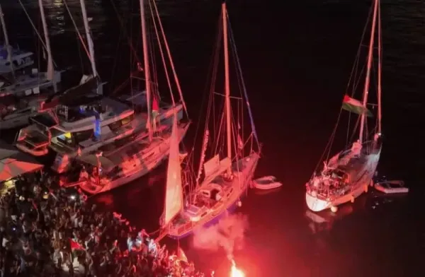 A screenshot from a drone video shows people lighting flares at the port of Ermoupolis during the departure of two sailing boats, Electra and Oxygen, part of the Global Sumud Flotilla aiming to reach Gaza (credit: REUTERS)