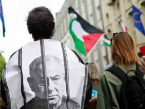 A pro-Palestinian activist is wrapped in an image depicting Prime Minister Benjamin Netanyahu behind bars as demonstrators march towards the Slovenian Prime Minister's Office, in Ljubljana, Slovenia, August 6, 2025. (credit: REUTERS/BORUT ZIVULOVIC)