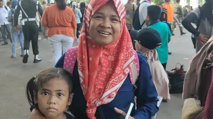 Sri Lestari, membawa serta anaknya ke HUT ke-80 TNI di Monas, Jakarta, Minggu (5/10/2025). Sri memperoleh kupon doorprize yang dibagikan oleh personel TNI dan berharap mendapatkan sepeda motor.