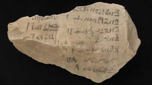 A receipt for making coffins 1530 to 1075BC made from limestone and with faded black ink writing. It is roughly diamond shaped and the writing is along its length. 

