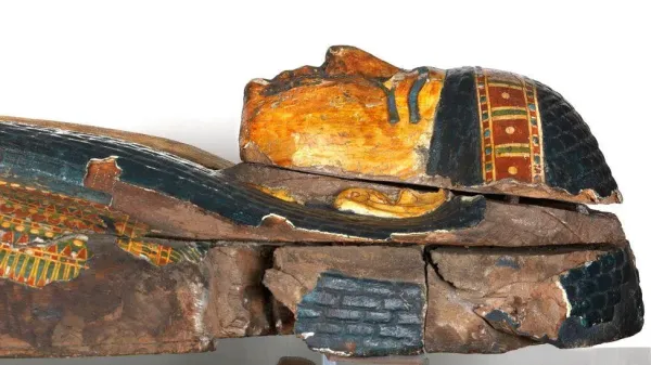 Head end of the inner coffin of the supervisor of scribes and of craftsmen’s workshops, Newpawershefyt, about 1000BC. It is made of wood and shows the head and the top of the torso and is lying on its back so it is in profile. The hair is painted black and braided, wtih a gold and red band across it. Its face is painted gold with its eyes highlighted in black. 