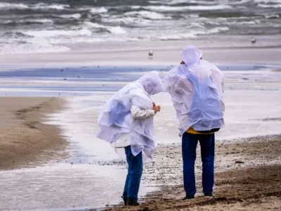 Walkers with rain protection search for amber in strong winds on the Baltic Sea beach at Warnemuende. Severe weather roiled Germany on Sunday, causing damage in several states and injuring at least two people - though on the coast, windsurfers embraced the conditions. Jens B&#xfc;ttner/dpa