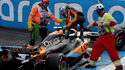 Oscar Piastri climbs out of his McLaren after crashing out on the first lap of the Azerbaijan Grand Prix. Two marshals are stood on either side of him, assisting him