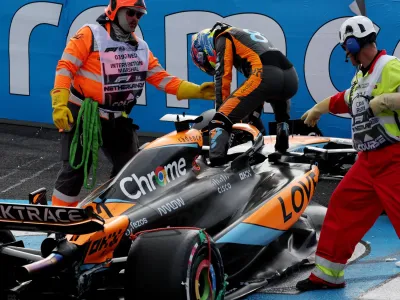 Oscar Piastri climbs out of his McLaren after crashing out on the first lap of the Azerbaijan Grand Prix. Two marshals are stood on either side of him, assisting him
