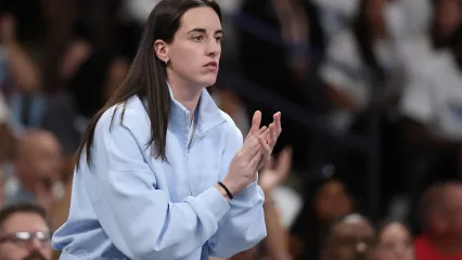 A woman in a light blue jacket watches a basketball game while clapping.