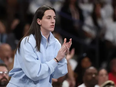 A woman in a light blue jacket watches a basketball game while clapping.