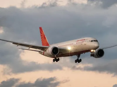 Stock picture of a large twin-engine aircraft in flight against a sky with light clouds. Its livery is the red and white of Air India 